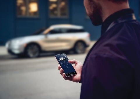 A person is shown interacting with a smartphone to connect to a Lincoln vehicle across the street. | McKie Lincoln, Inc. in Rapid City SD